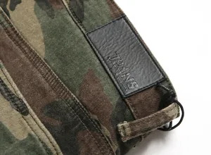 Detail of camouflage denim pants featuring a black embossed leather JEANS patch