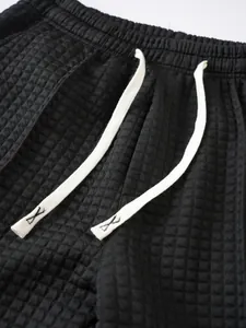 Detail view of black waffle knit pants featuring an elastic waist and white drawstrings.