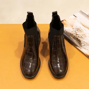 Detalle superior de botines de charol marrón oscuro con grabado de piel de cocodrilo.