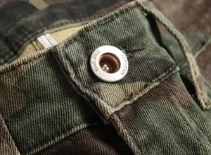 Macro detail of silver button on men's camouflage cargo denim pants with handmade engraving