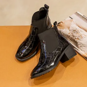 Detalle de botines de charol negro con estampado de cocodrilo y tacón grueso.