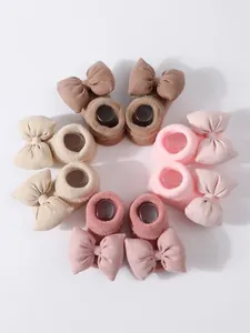 Juego de cuatro pares de calcetines gruesos para bebé con lazos en tonos neutros y rosas.