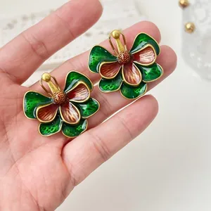 Boucles d'oreilles fleurs en émail vintage vert et rouge tenues en main pour l'échelle