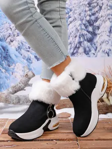 Close-up of black snow boots with white fur trim and thick platform soles in snow.