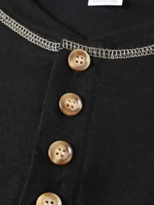 Détail d'un t-shirt Henley noir pour homme avec boutons marrons et coutures contrastées.