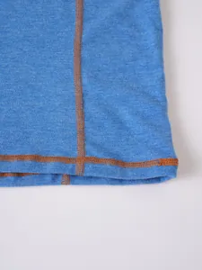 Détail macro montrant les coutures orange contrastées sur un t-shirt Henley bleu
