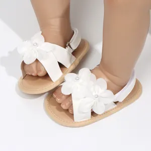Primo piano di eleganti sandali da principessa bianchi per neonata con fiori e perle