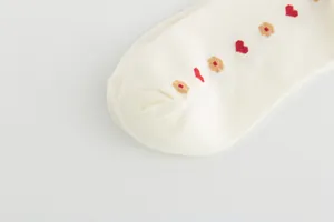 Detailed view of red heart and beige floral patterns on creamy white cotton socks fabric