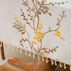 Close-up detail of elegant yellow floral embroidery and tassel fringe on a cream linen tablecloth