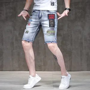 Detail of men's slim-fit light wash denim shorts with colorful embroidery and frayed hem