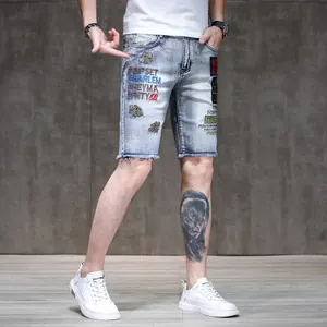 Detailed shot of men's slim denim shorts with embroidered patches and raw edges.