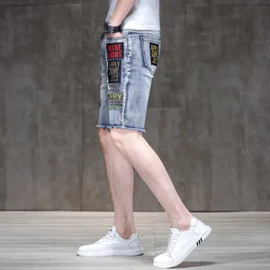 Side view of men's slim denim shorts with embroidered patches and raw frayed hems