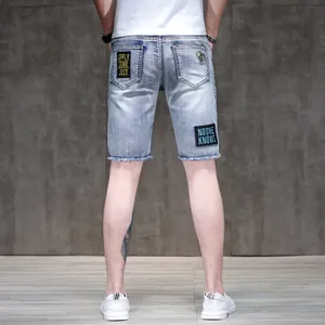 Back view of men's slim light blue denim shorts with embroidery patches and raw hem detail