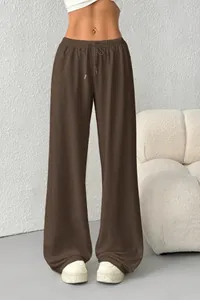 Brown wide-leg drawstring lounge pants shown in a modern minimalist indoor setting.
