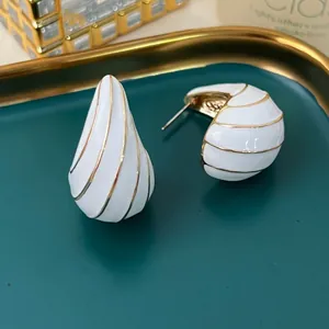 Detailansicht von weißen Emaille-Ohrringen in Tropfenform mit goldenen Akzenten.