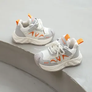 Baskets chunky pour enfants respirantes en blanc, gris et orange sur des marches.