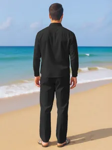 Full rear view of a man dressed in a solid black linen shirt and trousers set at the beach