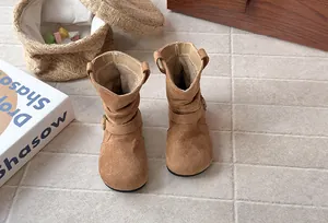 Vue détaillée de bottes plissées en daim marron pour filles sur un sol pavé.