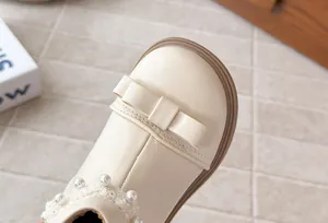 Gros plan détaillé de bottines beiges pour filles avec nœud, perles et dentelle.