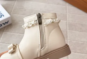 Détail de bottines pour filles en crème avec dentelle, perles et décoration de nœud.