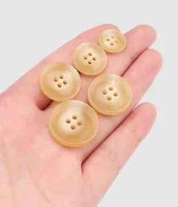 Macro view of five beige four-hole urea buttons in various sizes held in hand.