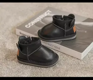 Detailed view of black children's winter snow boots with plush lining on a white prop book