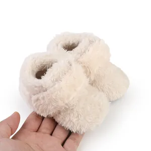 Close-up view of soft cream plush baby booties held by hand showing detailed furry texture