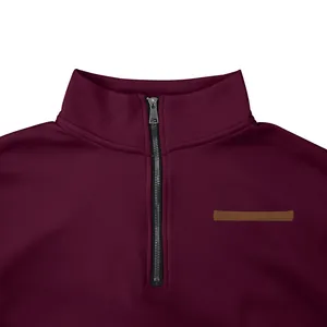 Zoom sur le col zippé et l'écusson de poitrine d'un sweat-shirt bordeaux.