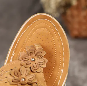 Detailaufnahme der Blumenverzierung und weißen Nähte an hellbraunen Strandsandalen.