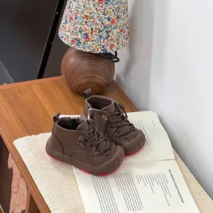 Warme braune Lederstiefel für Kleinkinder mit roten Sohlen auf einem Buch neben einer Lampe