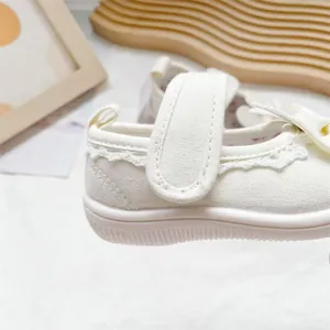 Close-up detail of elegant white toddler canvas shoes featuring lace trim and velcro strap.