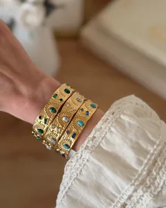 Close-up of three gold stainless steel floral bangles with colorful stones worn on a wrist.