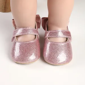 Close-up of pink glitter baby walking shoes with bow detail for infants 3-12 months.