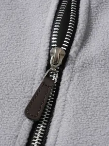 Close-up detail of metal half-zipper with brown puller on grey fleece sweatshirt