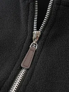 Detailed macro view of the metal zipper and brown leather pull on a black fleece top
