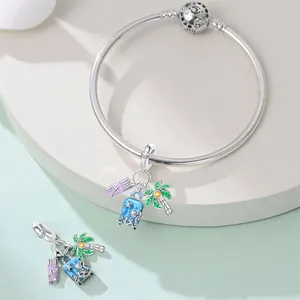Detailed view of travel-themed silver charms with palm tree and suitcase on a bangle.
