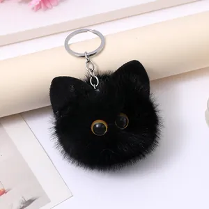 Detailed close-up of a fuzzy black cat head keychain with large yellow eyes and fluffy fur