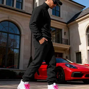 Full view of black cable knit tracksuit on model beside red luxury sports car