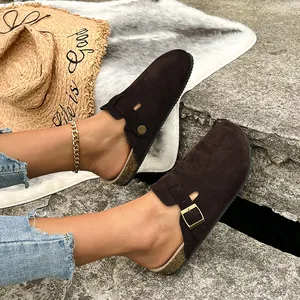 Primo piano di sabot in pelle scamosciata marrone con fibbia su sfondo di pietra