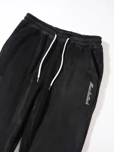 Close-up of men's black fleece joggers with white drawstring and embroidery detail.