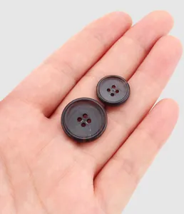 Detailed macro view of premium dark brown resin four-hole buttons held in a human hand