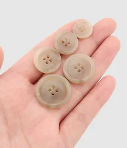 Vue détaillée de boutons en résine beige de différentes tailles tenus dans la main
