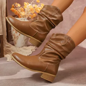 Elegantes botas de vaquero retro marrones con pliegues y tacón ancho usadas por una modelo.