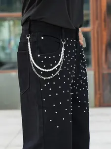 Detail of men's black jeans with rhinestone studs and pearl chain accessory