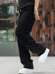 Detail view of men's loose black straight jeans featuring heavy silver rhinestone studs.