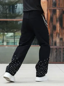 Detail view of men's black straight jeans with sparkling rhinestone studs on lower leg