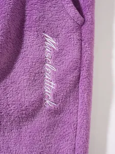 Detailed view of the white Muscleattack embroidery on soft purple fleece jogging pants