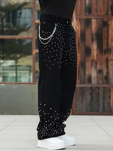 Close-up detail of black baggy jeans featuring sparkling rhinestone studs and chain.