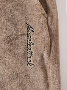 Close-up of men's plush fleece joggers featuring black script embroidery detail.