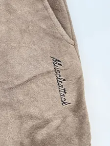Detail view of premium black 'Muscleattack' cursive embroidery on soft taupe fleece joggers